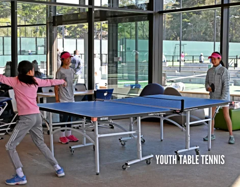 Youth table tennis players practicing indoors at the Goldman Tennis Center during a youth table tennis program through Lifetime Activities.